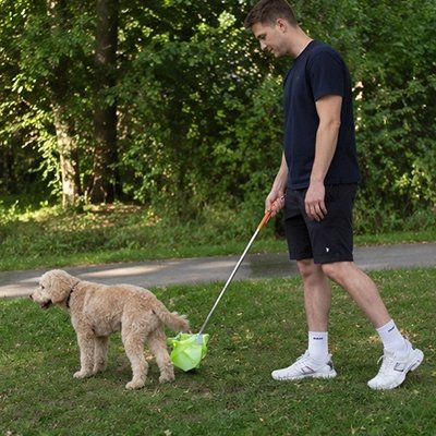 Ramasse crotte chien​ homme suivant son chien avec le ramasse crottes pour recueillir ses excrément durant la promenade